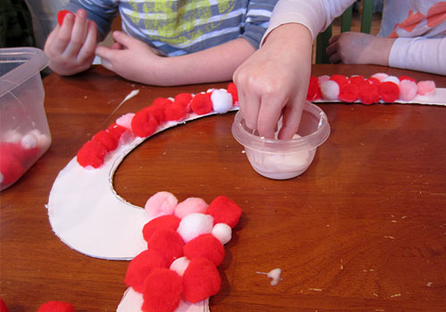 Do you love homemade Valentine's Day kids crafts? We sure do! This brightly colored Pom Pom Wreath is full of whimsy and sensory fun!